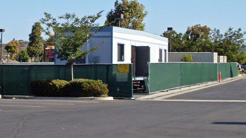 Portable fence panels near Morro Bay, California, with green privacy screen surrounding a construction office.